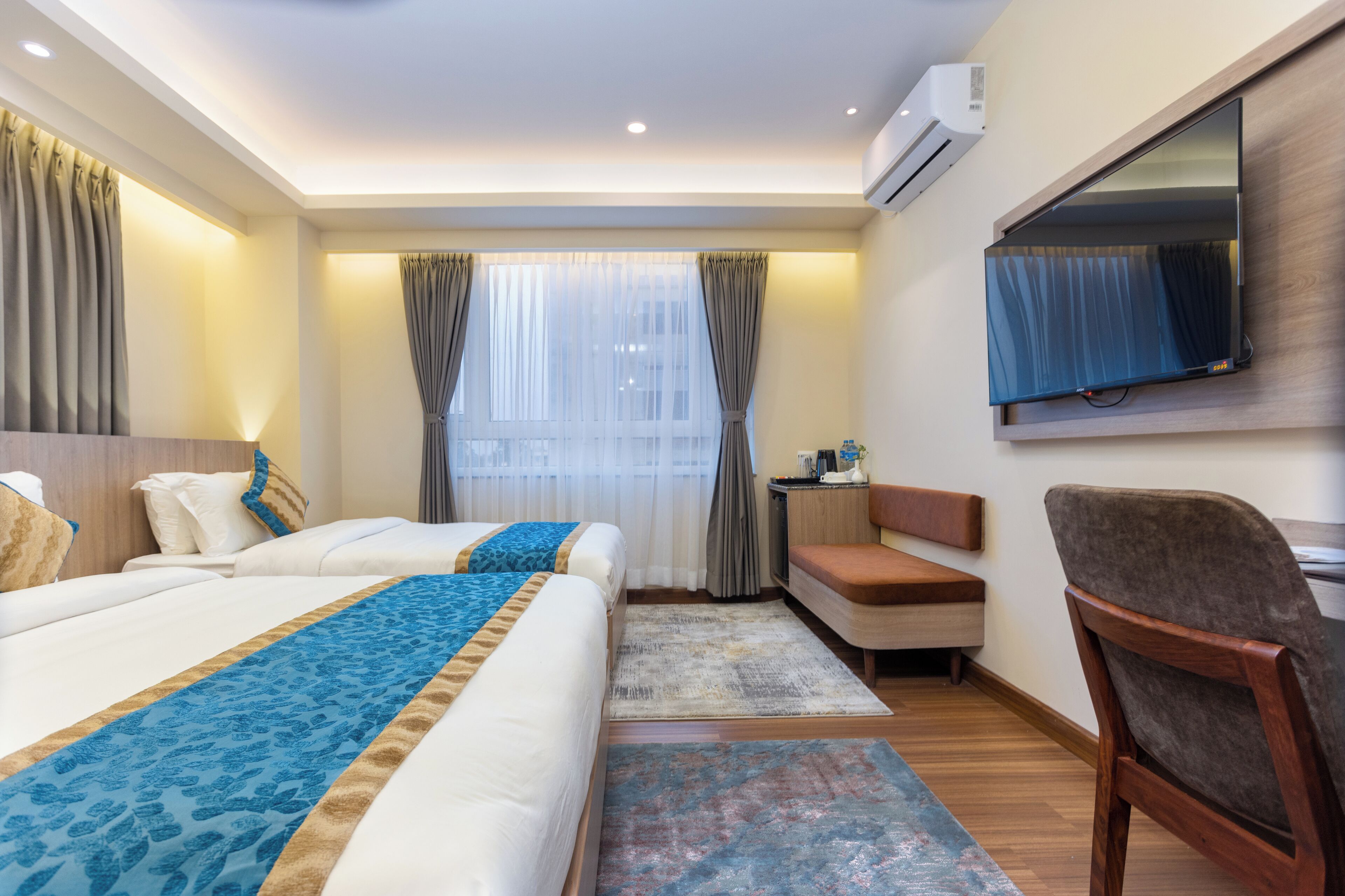 A hotel room with two beds, a desk, a chair, a TV, and a window with curtains.
