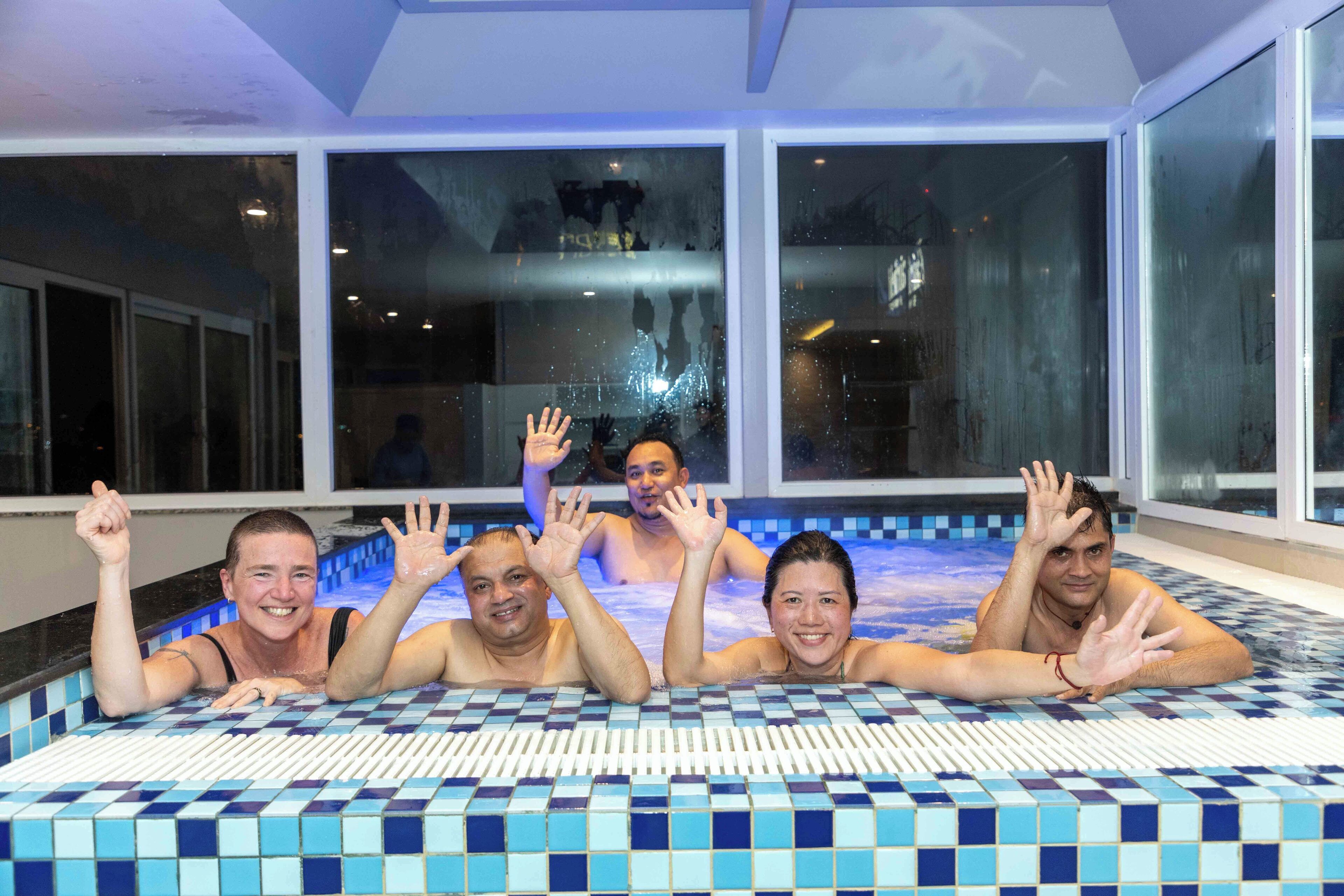 A group of people in a tiled indoor swimming pool with large windows.