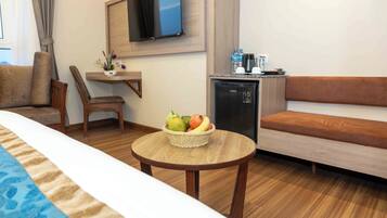 Una habitación de hotel con una cama, una mesa de madera con una cesta de frutas, un sofá, una silla, un televisor montado en la pared y un minibar.