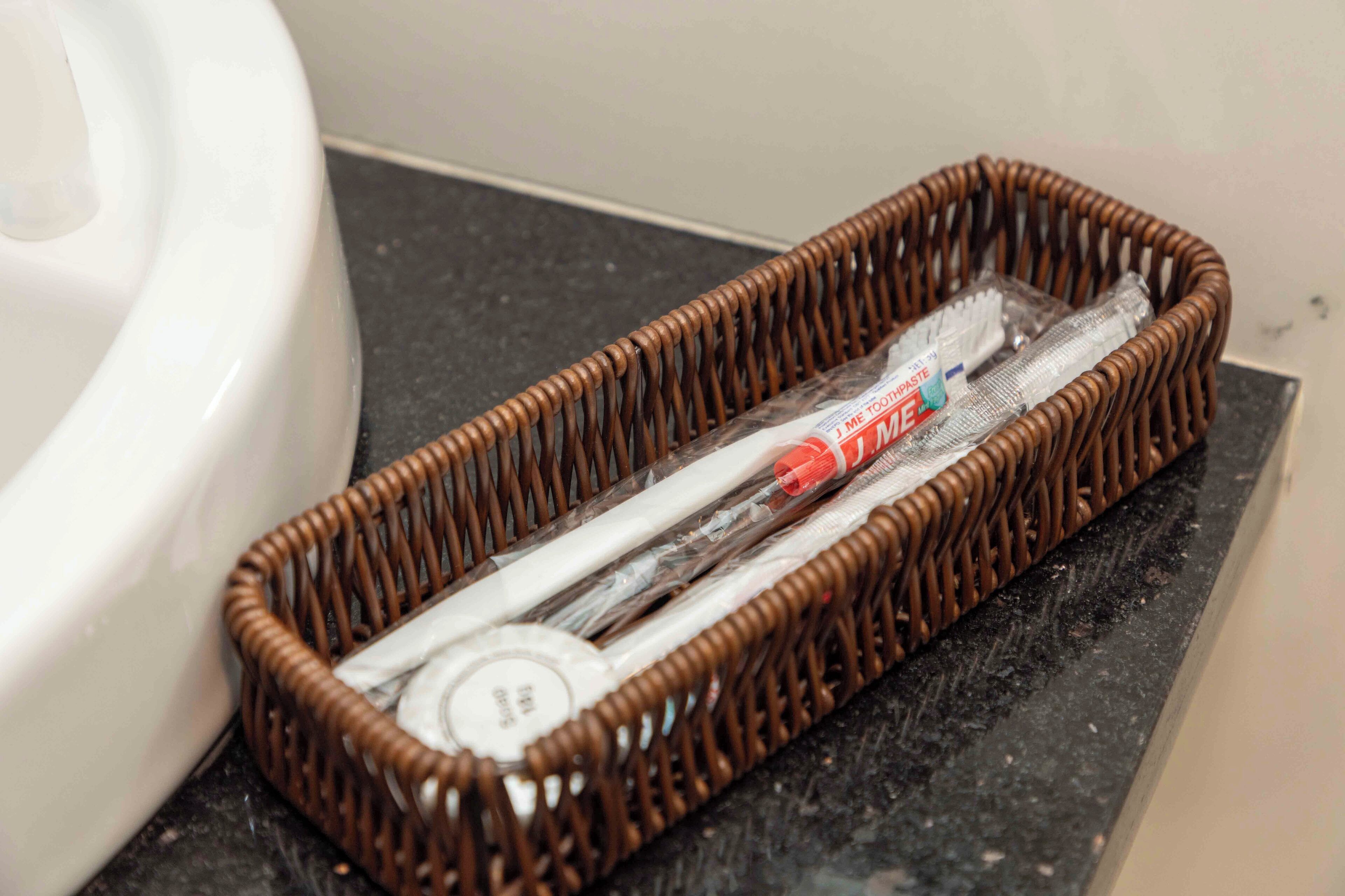 A wicker basket containing toothbrushes and toothpaste on a bathroom counter.