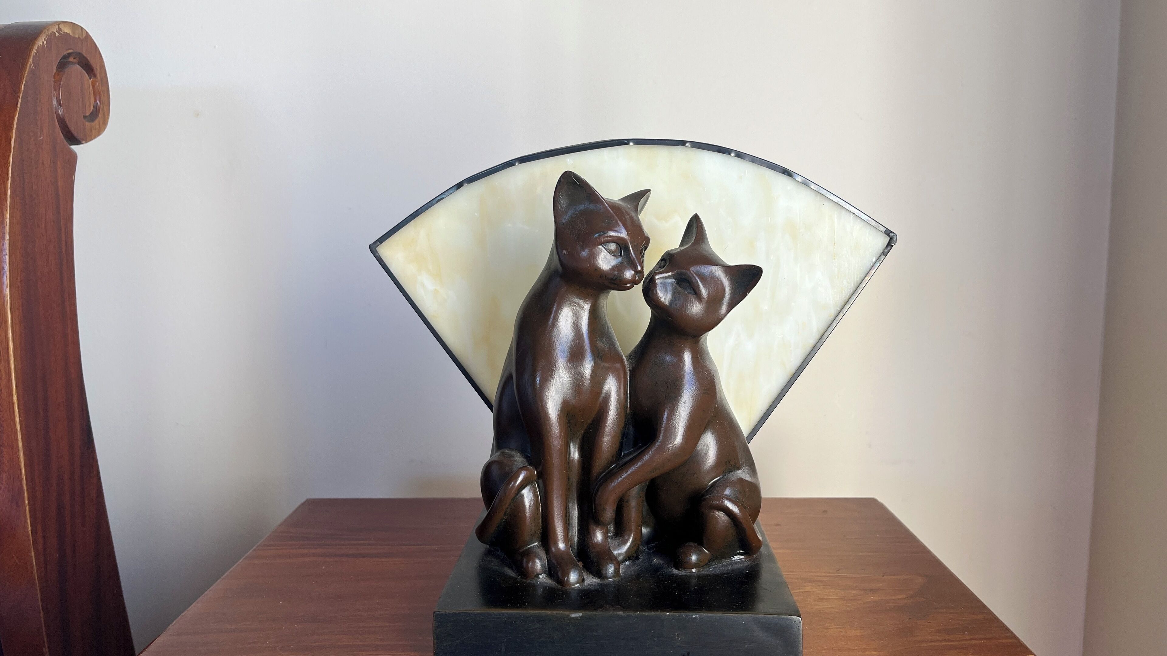 Una mesa de madera con acabado marrón oscuro, una escultura de dos gatos en marrón oscuro, y un abanico blanco semitransparente.