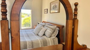 A bedroom with a wooden four-poster bed, a quilted bedspread, and two pillows. There is a window with a view of greenery outside. - Self contained cabin in quiet coastal bushland setting. Pet friendly! (Robe)