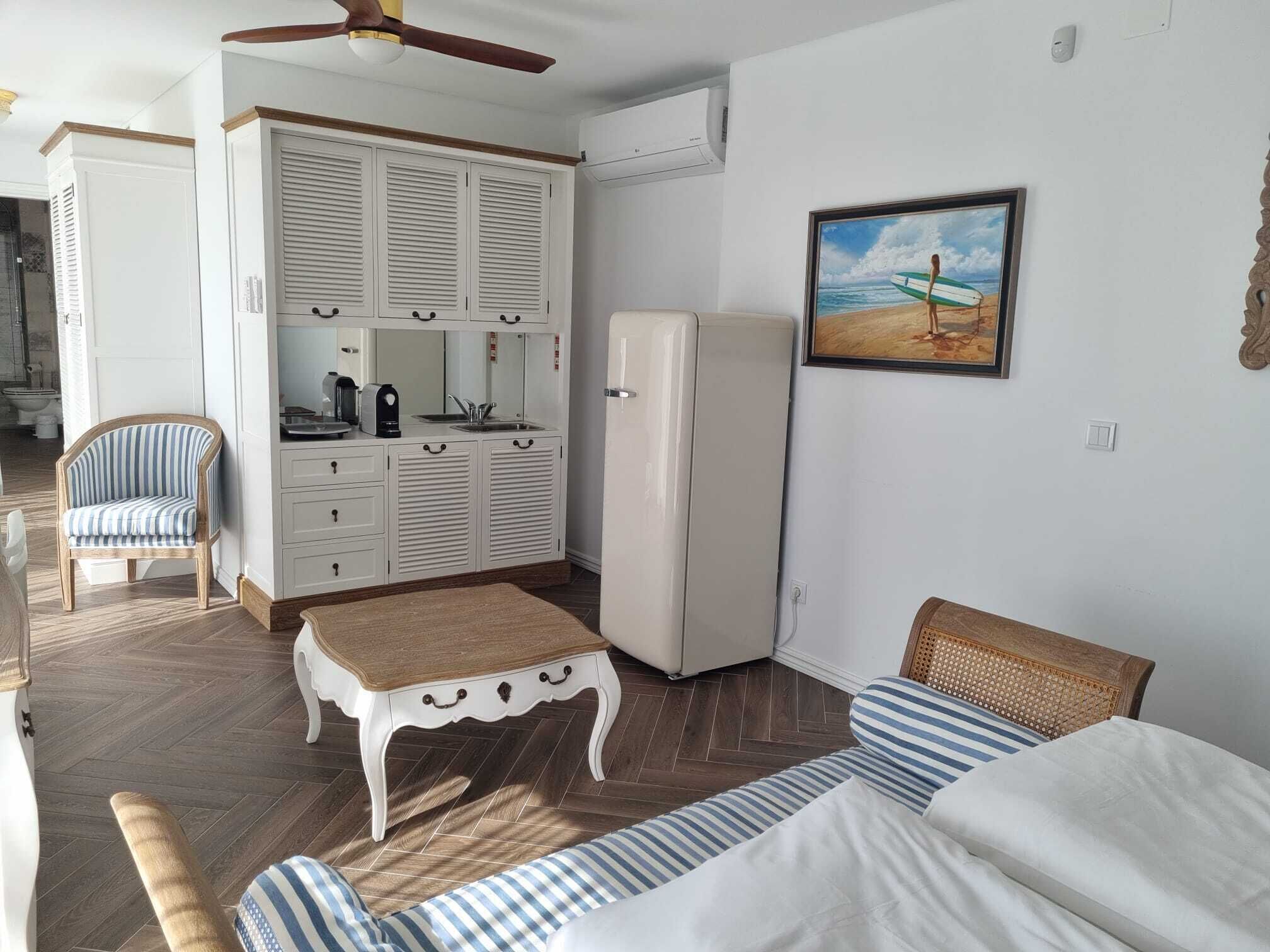 A bedroom with a bed, a small table, a chair, a wardrobe, and a refrigerator.