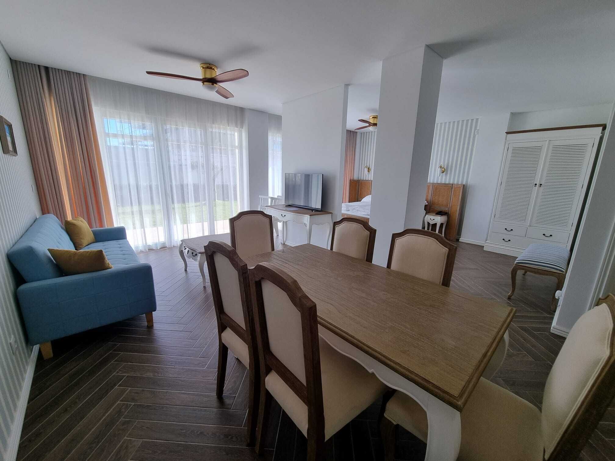 A dining area with a wooden table and chairs, a blue sofa, and a television.