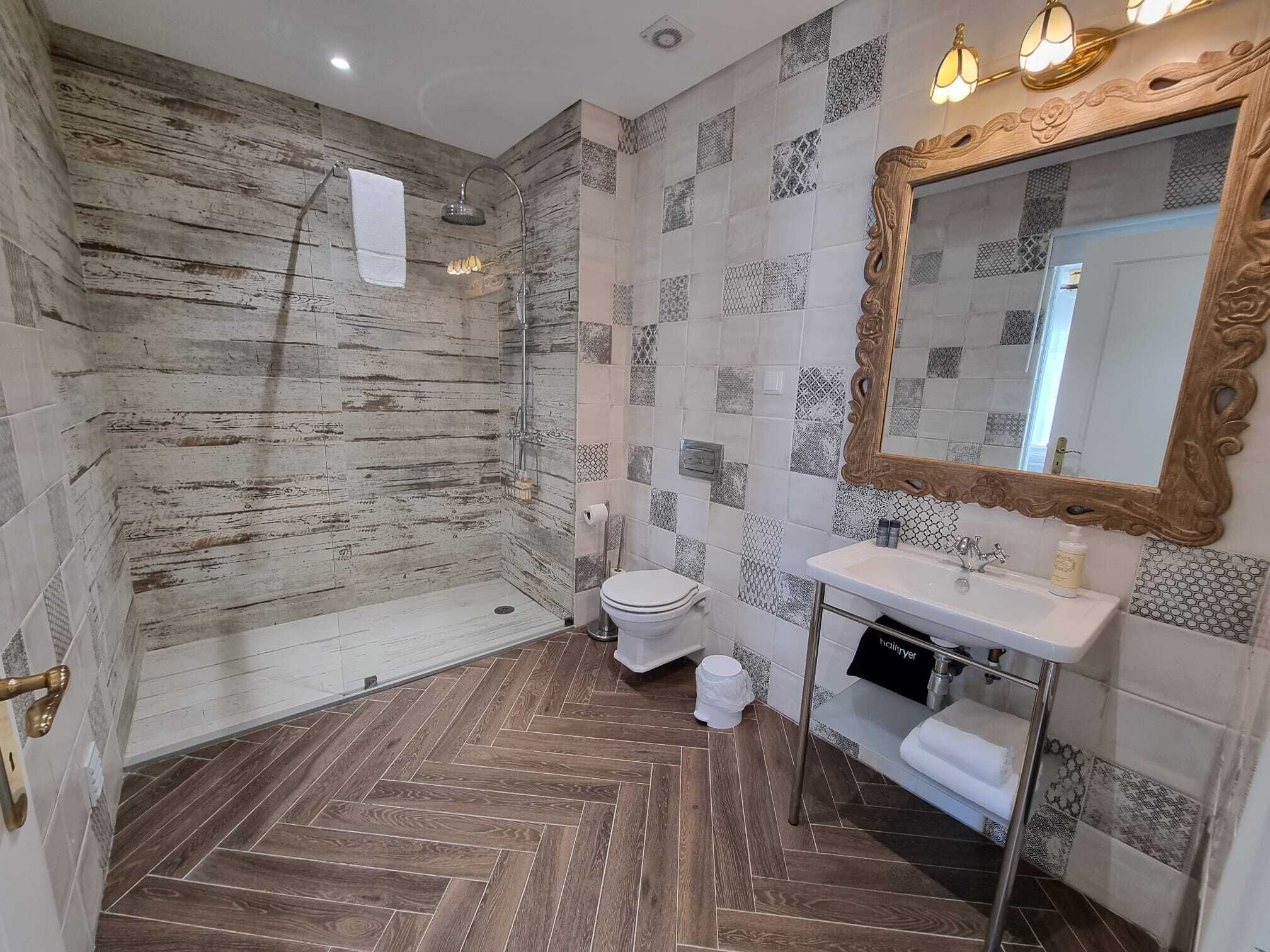 Un baño con ducha, inodoro, tocador y un espejo grande.