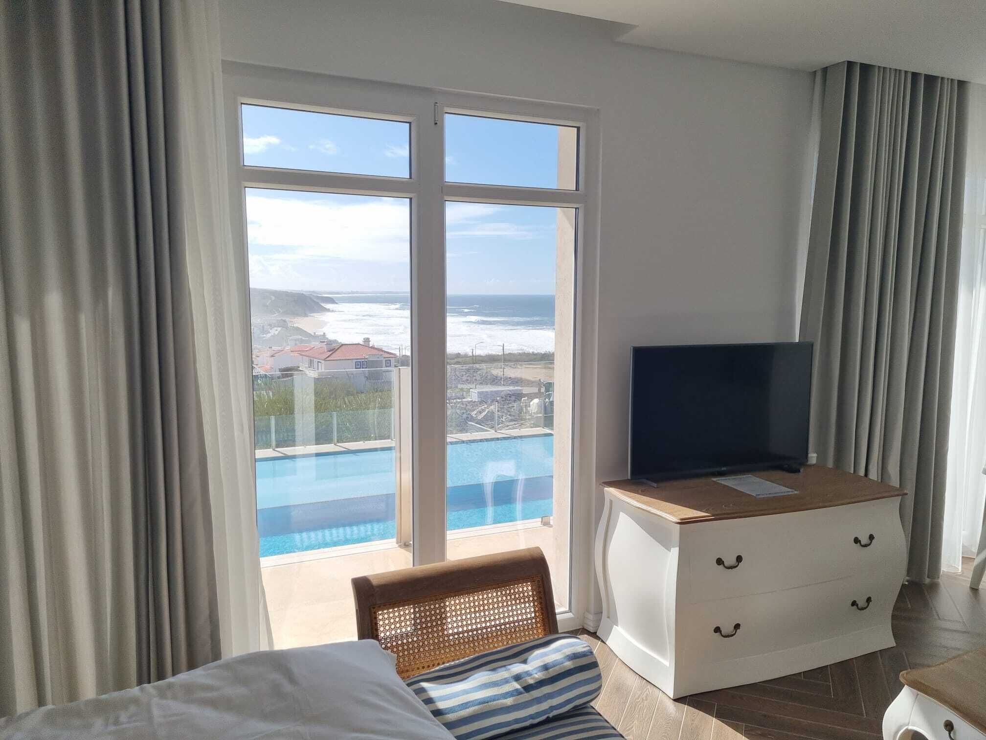 Hotelkamer met groot raam, uitzicht op zwembad en zee.