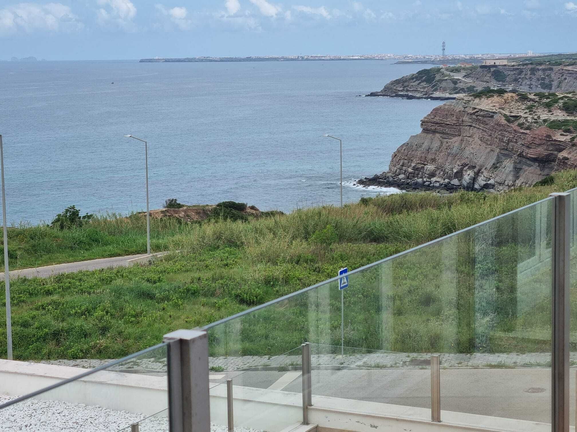 A coastal view with a road, grassy area, and rocky cliffs.
