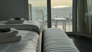 A hotel room with two beds, a view of the sea, and a balcony with a table and chairs. - Ocean View Apartments - Ocean View (Lourinha)