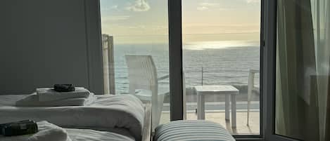 A hotel room with two beds, a view of the sea, and a balcony with a table and chairs.
