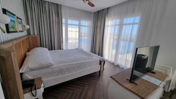 A hotel room with a bed, a wooden headboard, a ceiling fan, a TV, and a view of the outdoors.