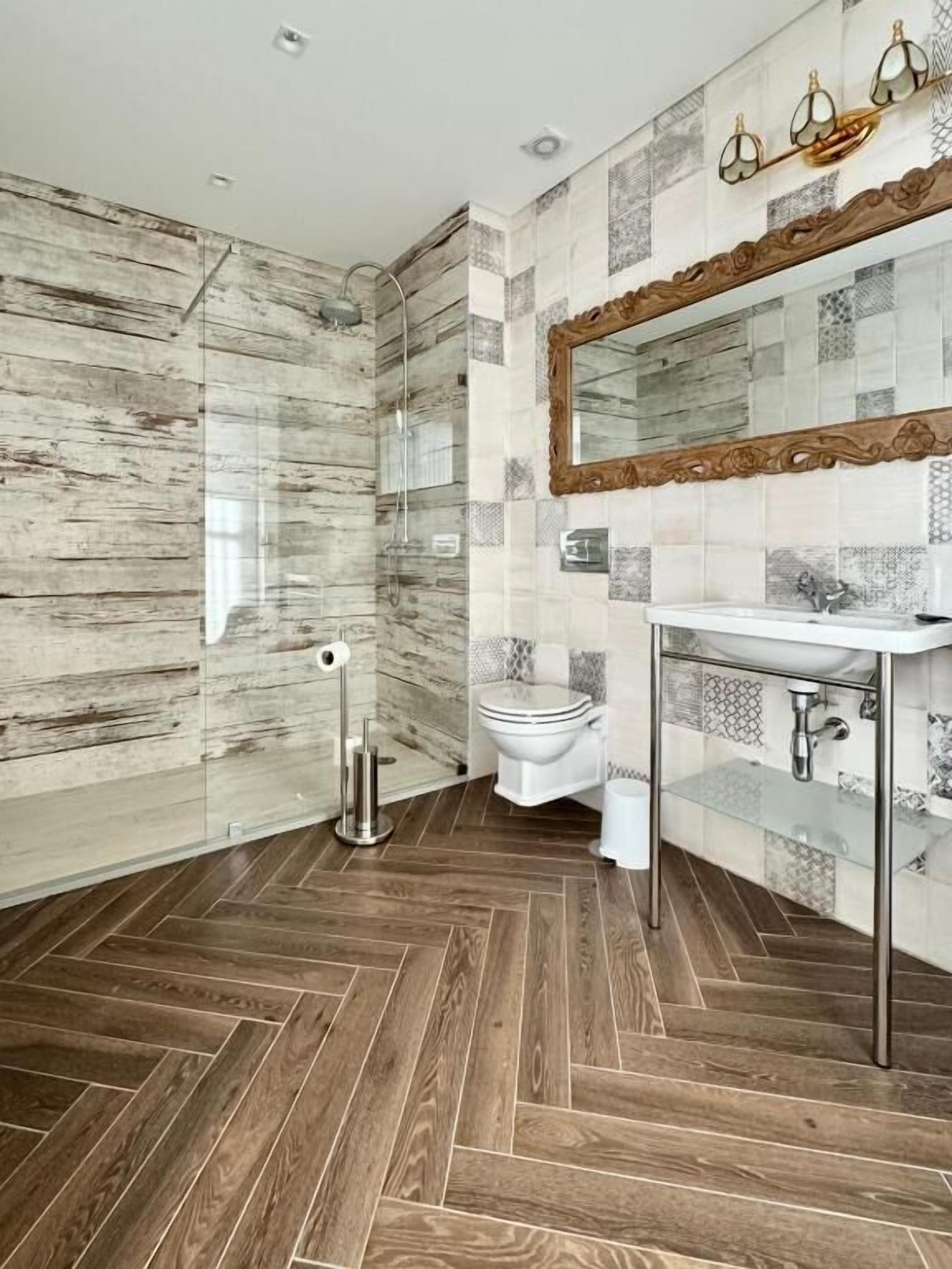 Ein modernes Badezimmer mit Holzboden, einer Glasdusche, einer weißen Toilette und einem Waschtisch mit Spiegel.