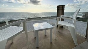A balcony with a view of the ocean, featuring two white chairs and a small table. - Ocean View Apartments - Ocean View (Lourinha)