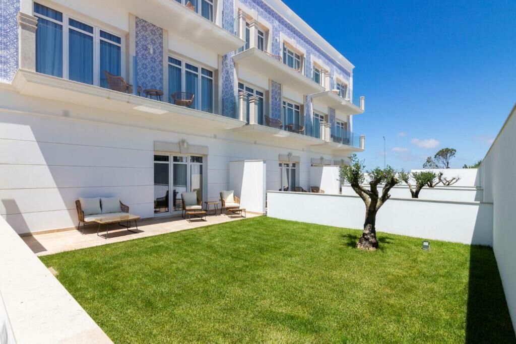 A modern building with a white exterior, multiple balconies, and a well-maintained lawn.