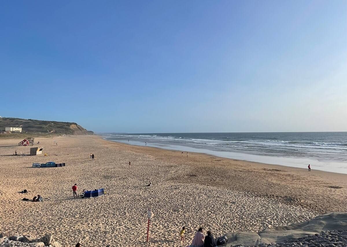 En bred sandstrand med några få personer och lite strandutrustning.