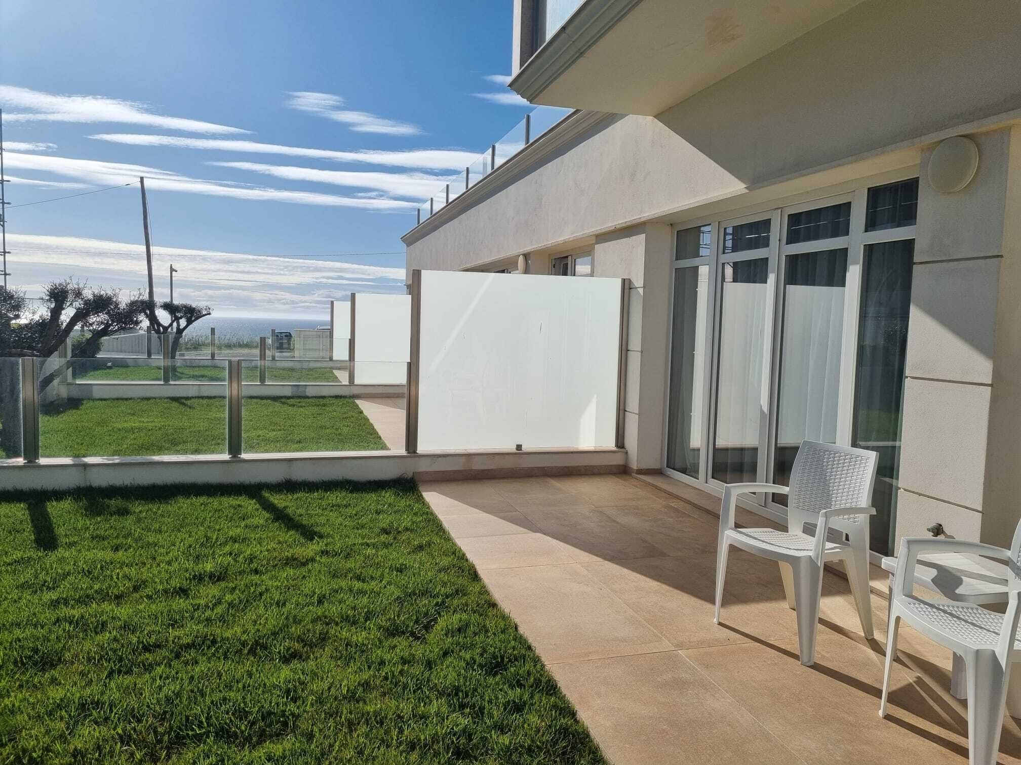 Ein modernes Gebäude mit flachem Dach, großen Fenstern und einer Terrasse mit Stühlen und Tisch.