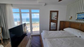Una camera d'albergo con un letto, una televisione, un'ampia finestra vista spiaggia e una ventola a soffitto.