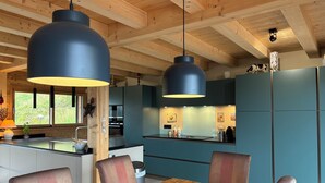 A modern kitchen with wooden beams, teal cabinets, and a wooden dining table with chairs. - New luxury chalet in Morzine's La Cote d'Arbroz with a Jacuzzi, beautiful views, and a quiet setting (La Côte-d'Arbroz)