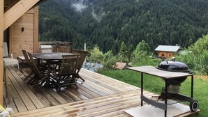 A wooden deck with a table and chairs, a barbecue grill, and a view of a forested mountain. - New luxury chalet in Morzine's La Cote d'Arbroz with a Jacuzzi, beautiful views, and a quiet setting (La Côte-d'Arbroz)