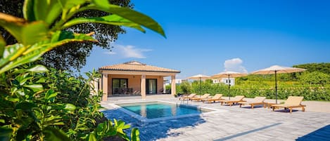 A pool area with lounge chairs and a building with a tiled roof.