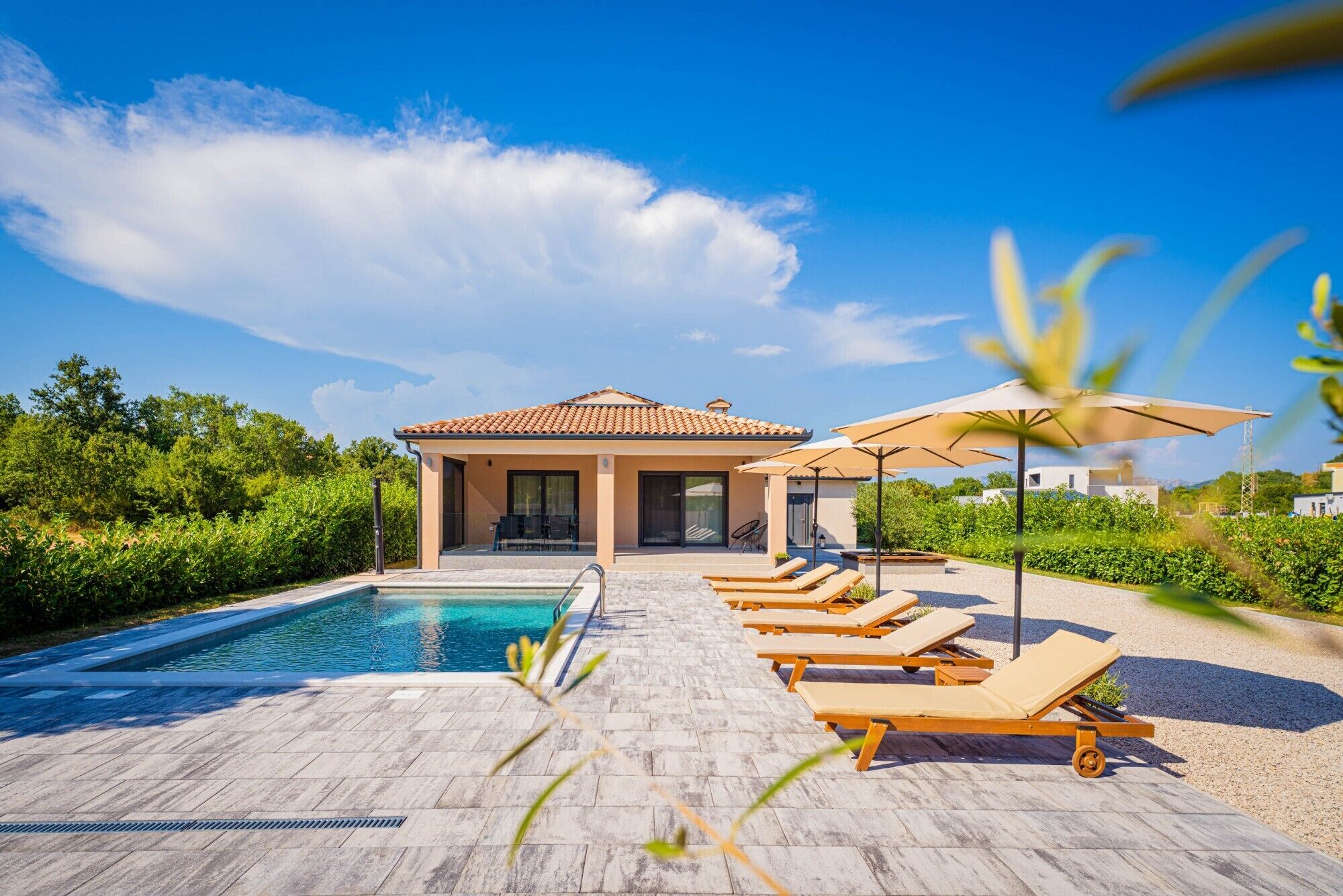 A pool area with lounge chairs and umbrellas, a covered seating area, and a building with a tiled roof.