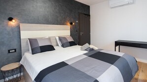 A modern bedroom with a large bed, a small round table, a desk, and a wardrobe.