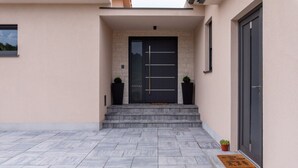 A modern building entrance with a black door, stone steps, and potted plants.