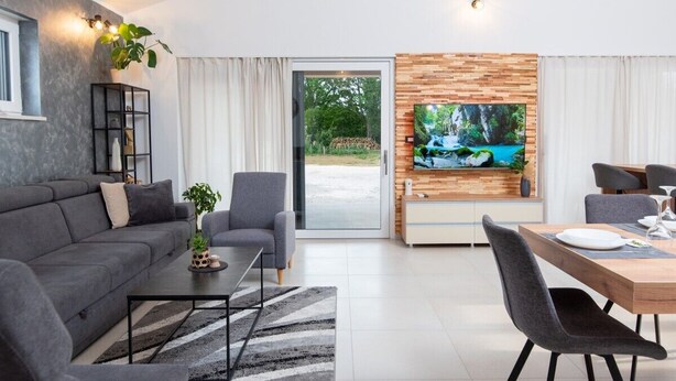 A modern living room with a grey sofa, a coffee table, and a dining area with a wooden table and chairs.