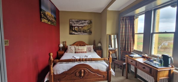 A bedroom with a wooden bed, a desk, and a view of the countryside through large windows. - Corsewall Lighthouse Hotel (Stranraer)