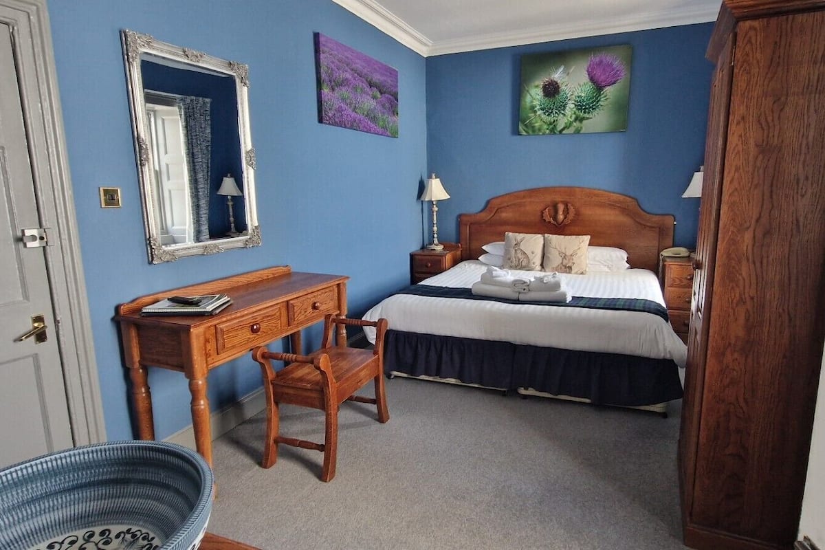 A bedroom with a bed, bedside table, lamp, and a desk with a chair.