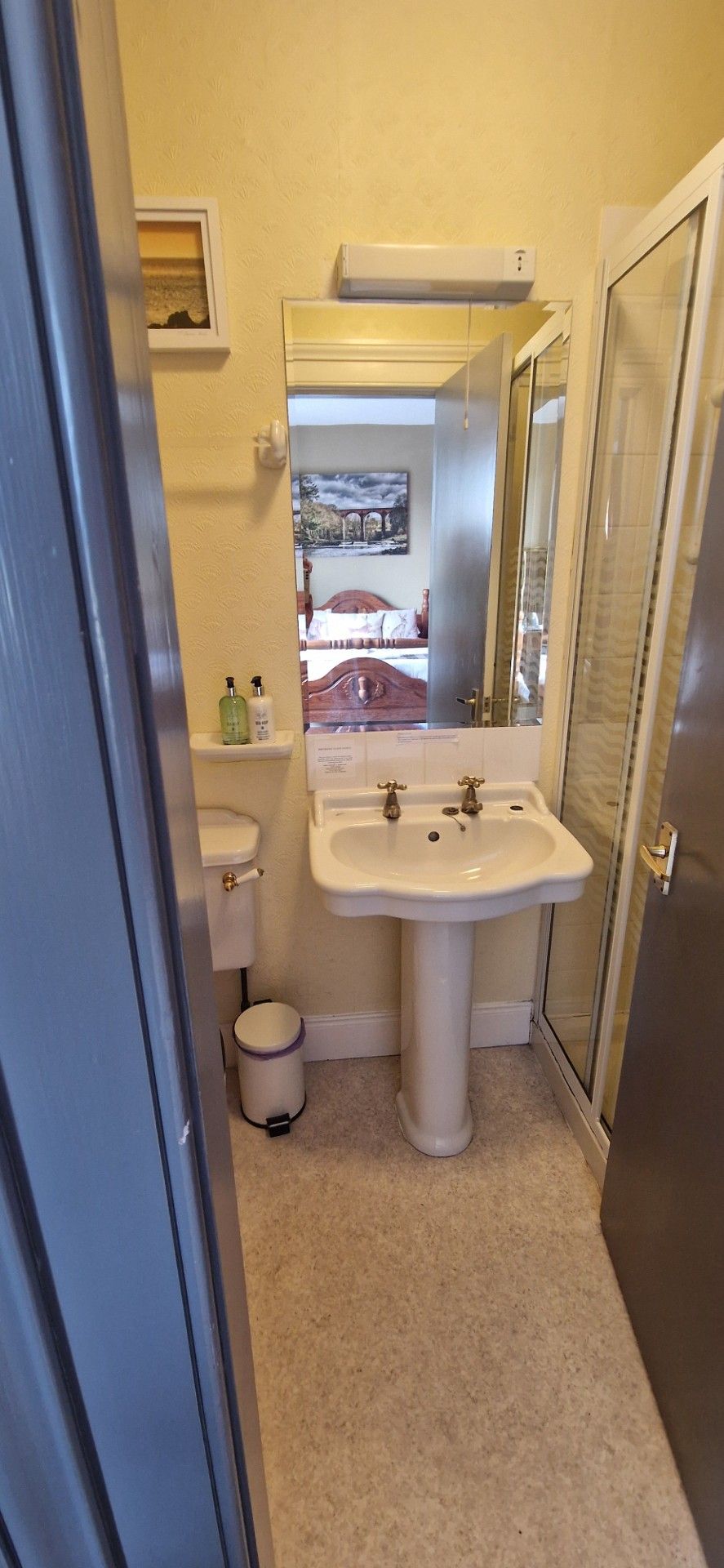 A bathroom with a pedestal sink, toilet, and a small trash bin.