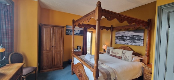 A four-poster bed with a wooden frame, a wardrobe, a desk with a chair, and a painting on the wall. - Corsewall Lighthouse Hotel (Stranraer)