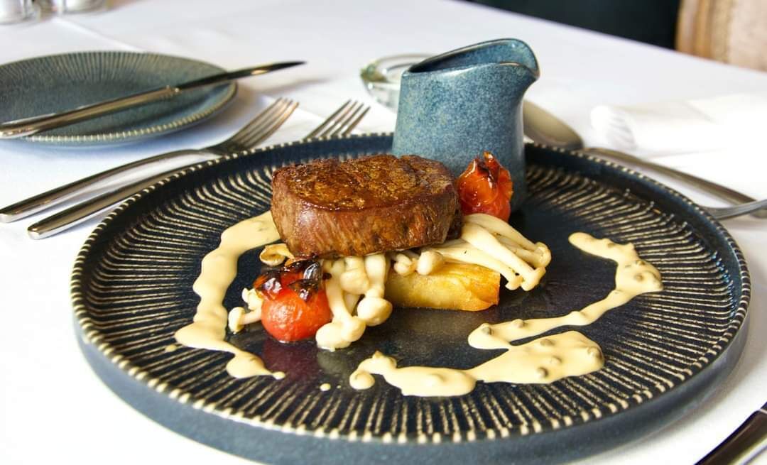 Un plato con un bistec, tomates cherry y una salsa.