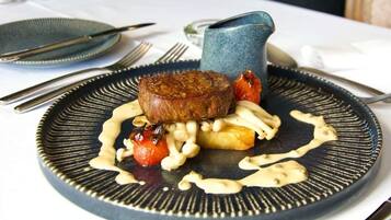 A plate with a steak, cherry tomatoes, and a sauce.