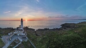 A lighthouse on a rocky coastline with a clear view of the sunset over the water. - Corsewall Lighthouse Hotel (Stranraer)