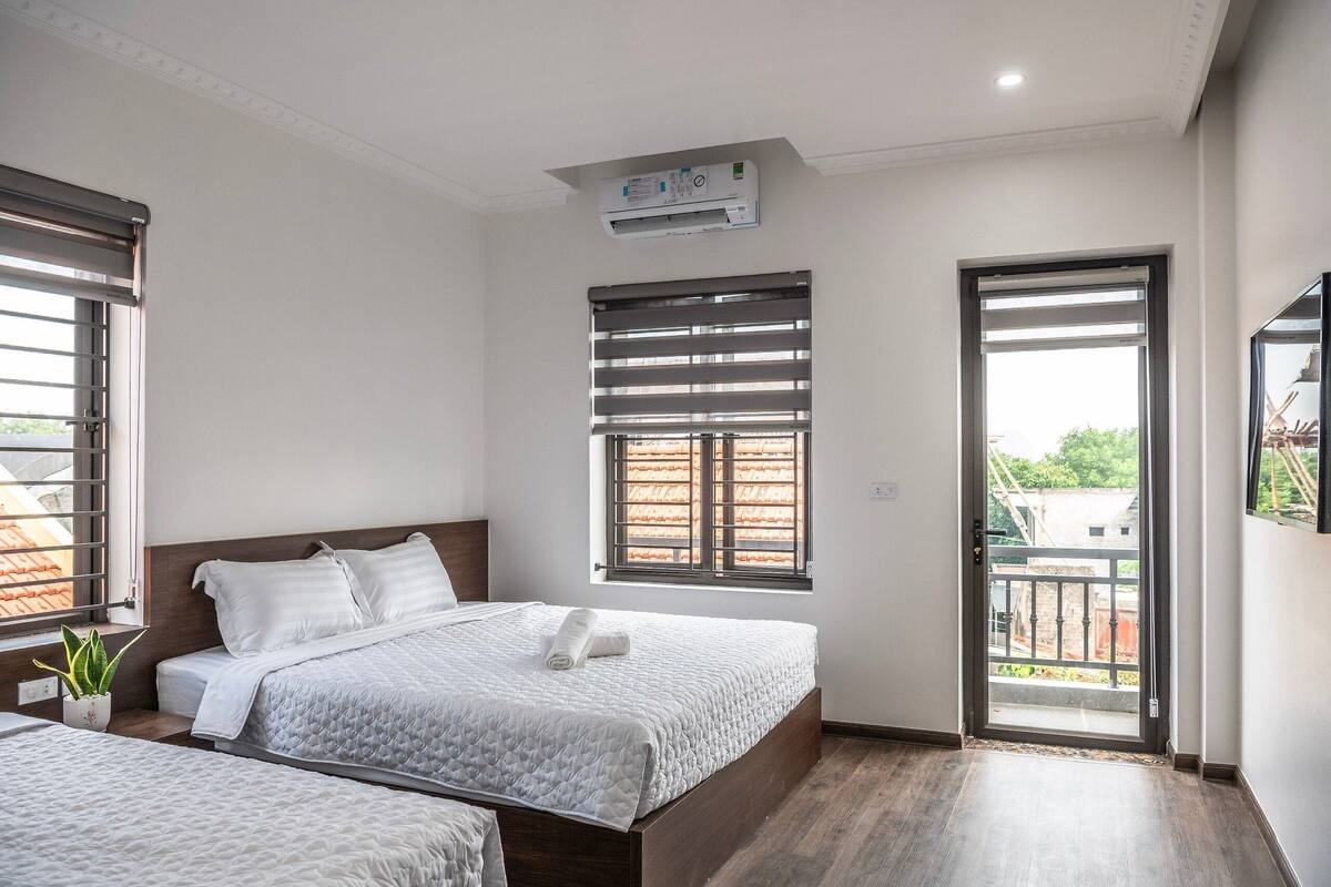 A bedroom with two beds, a window with blinds, an air conditioning unit, and a balcony door.
