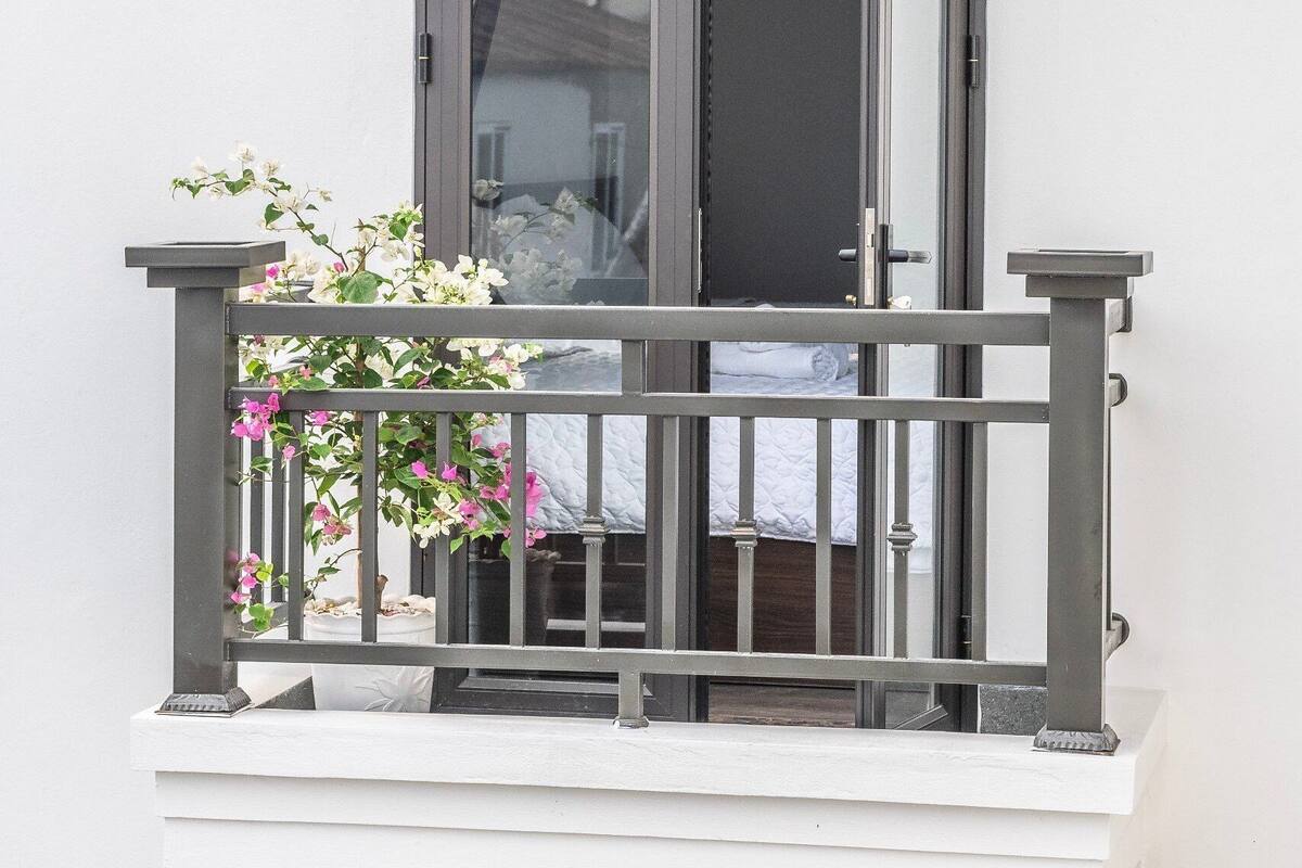 A balcony with a metal railing, a small table, and a potted plant with pink flowers.
