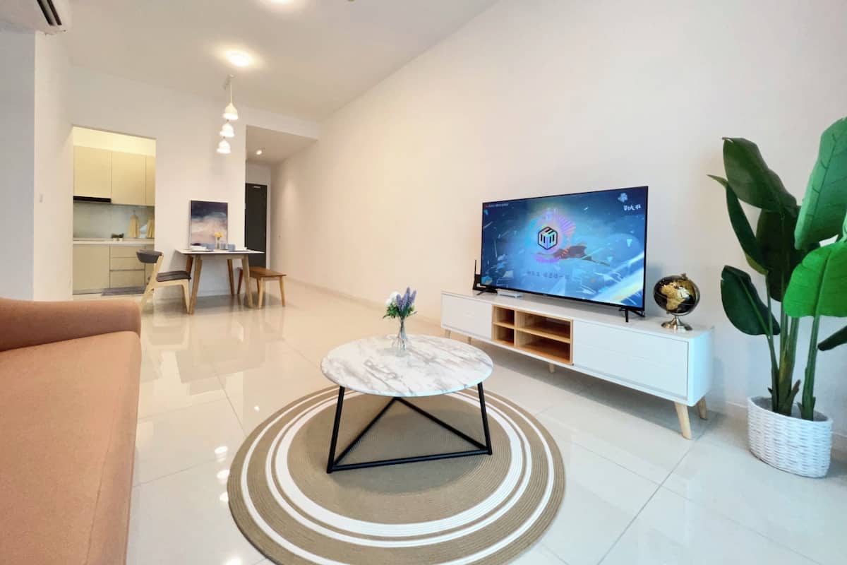 Ein modernes Wohnzimmer mit Flachbildfernseher, rundem Couchtisch, einer Couch und einem Essbereich im Hintergrund.