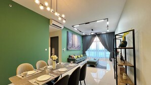 A modern dining area with a long table set for four, a sofa, and a bookshelf. - Paradigm Residence By Antlerzone (Johor Bahru)