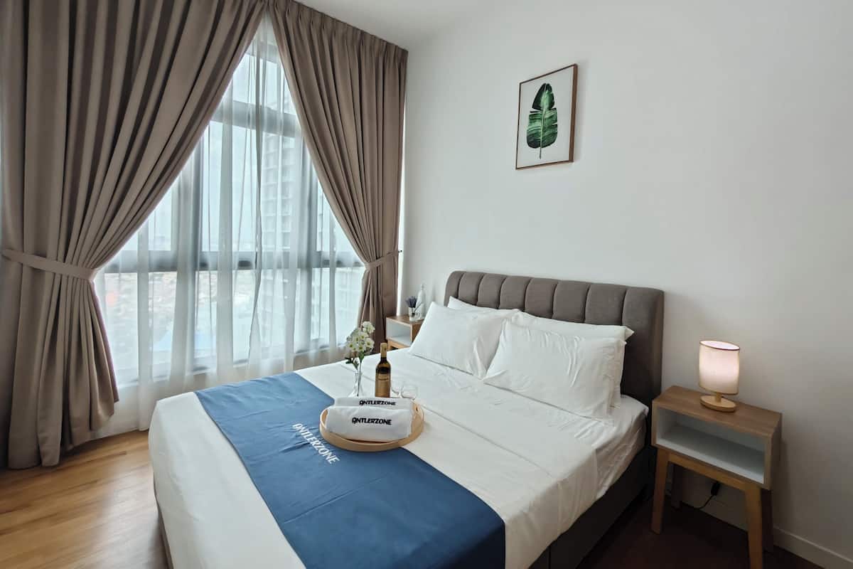 Ein Hotelzimmer mit einem großen Bett, einem Nachttisch mit Lampe und einem Fenster mit Vorhängen.