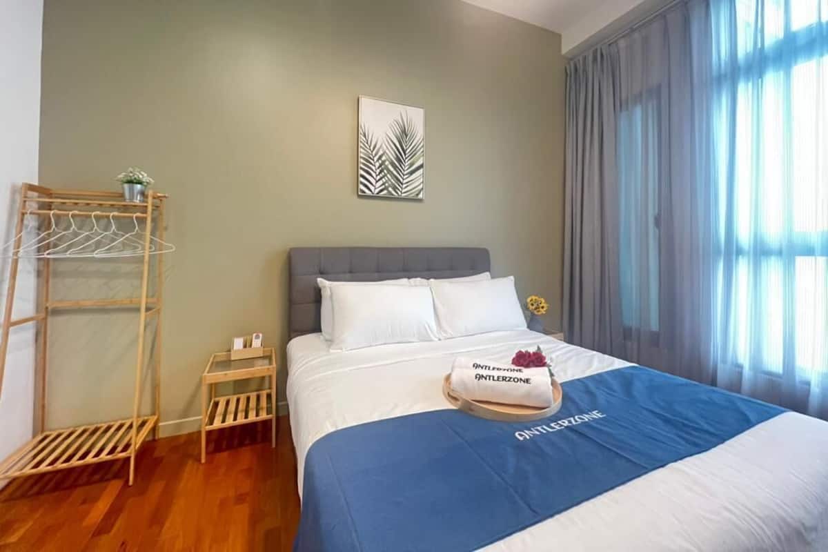 Ein Hotelzimmer mit einem Bett, einer an der Wand befestigten Pflanze, einem kleinen Tisch mit Pflanze und einem Fenster mit Vorhängen.