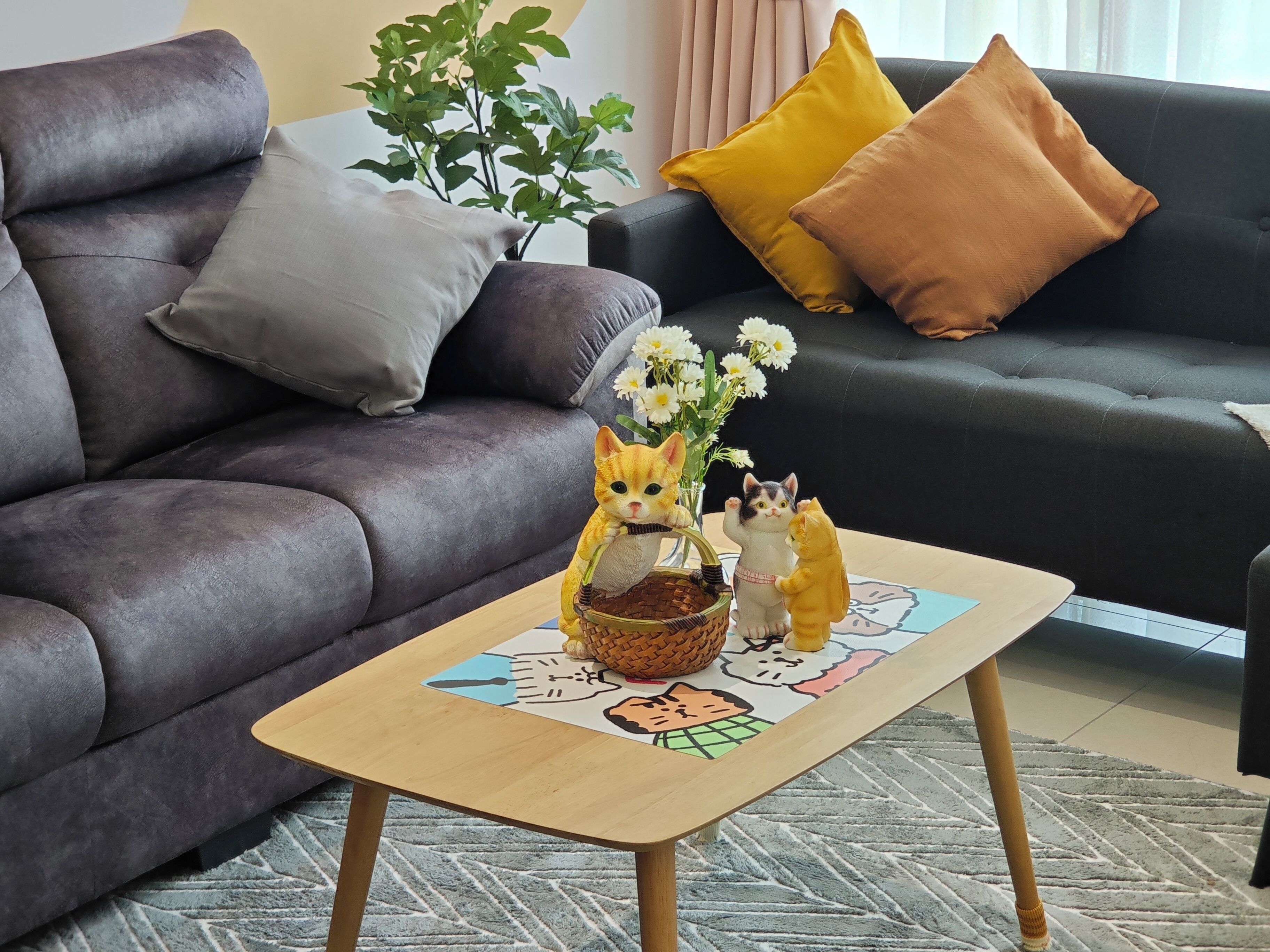 Una sala de estar con un sofá gris oscuro, una mesa de centro de madera con una figurita de gato, una planta y un jarrón con flores.