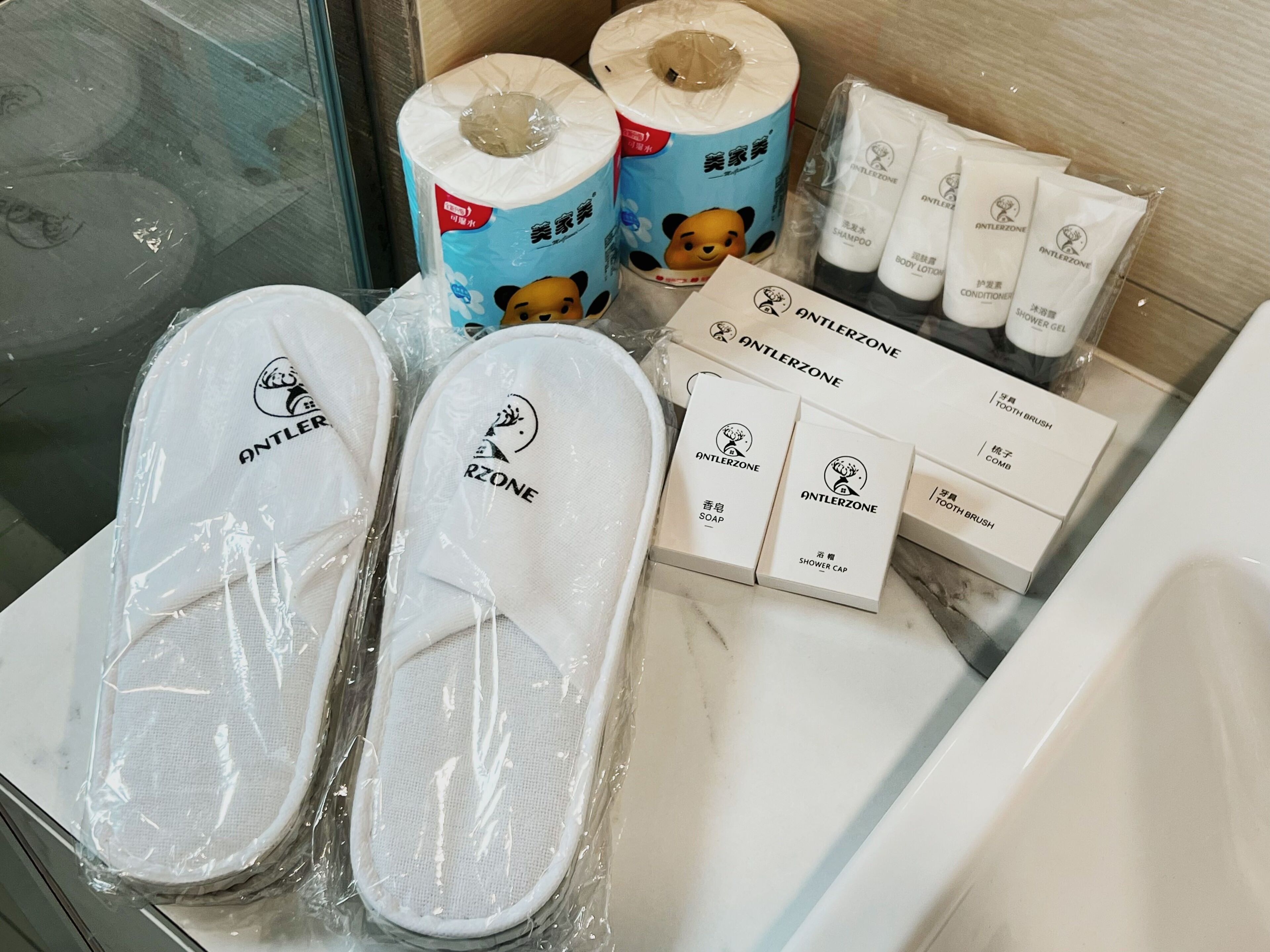 Baño con artículos de aseo que incluye pantuflas, papel higiénico, champú, acondicionador, loción corporal, gorro de ducha y jabón.