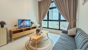 A modern living room with a flat-screen TV, wooden entertainment unit, a round coffee table, a grey sofa, and a large window with curtains. - Paradigm Residence By Antlerzone (Johor Bahru)