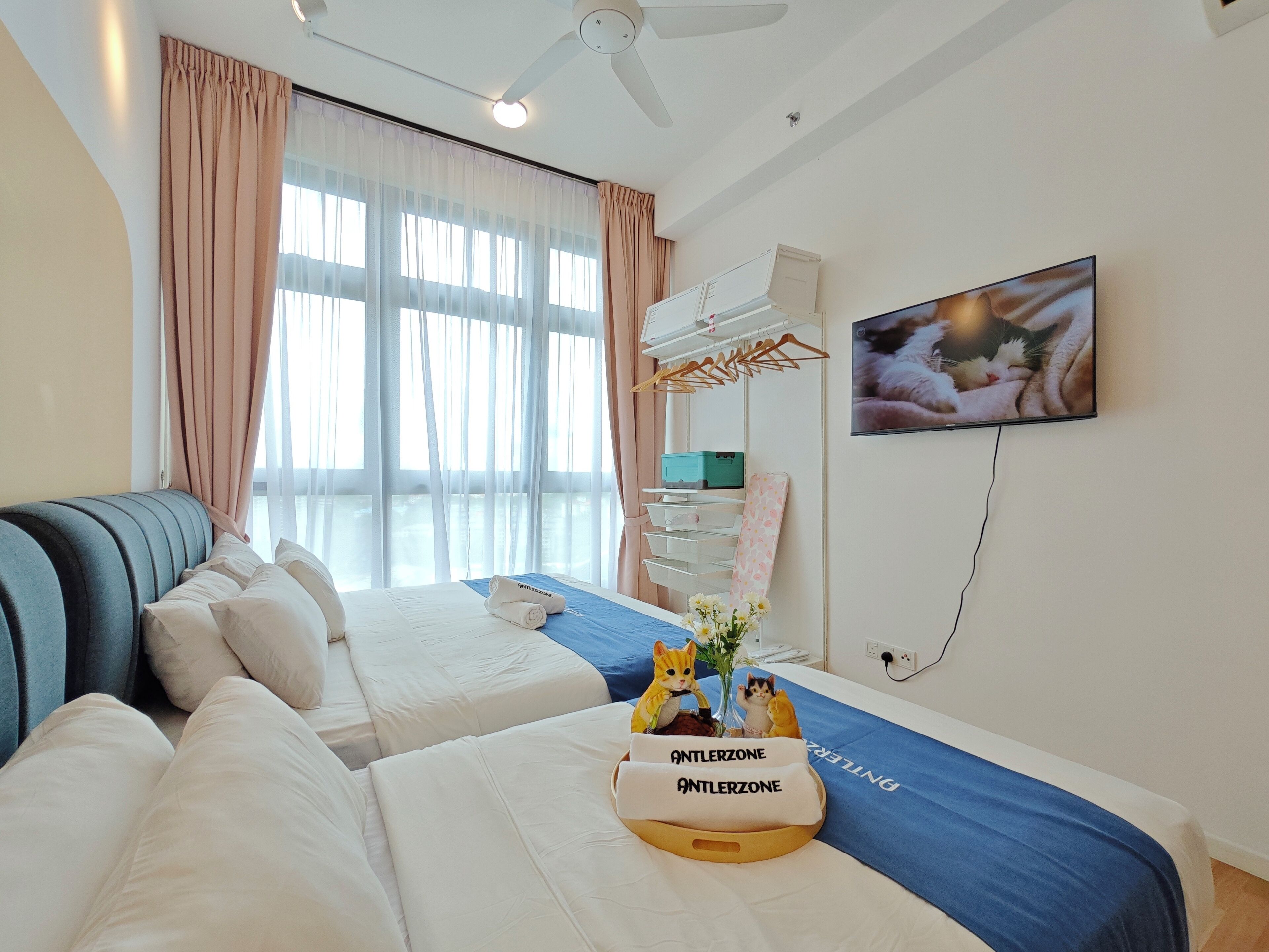 Habitación de hotel con dos camas, televisión, ventilador de techo y ventana con cortinas.