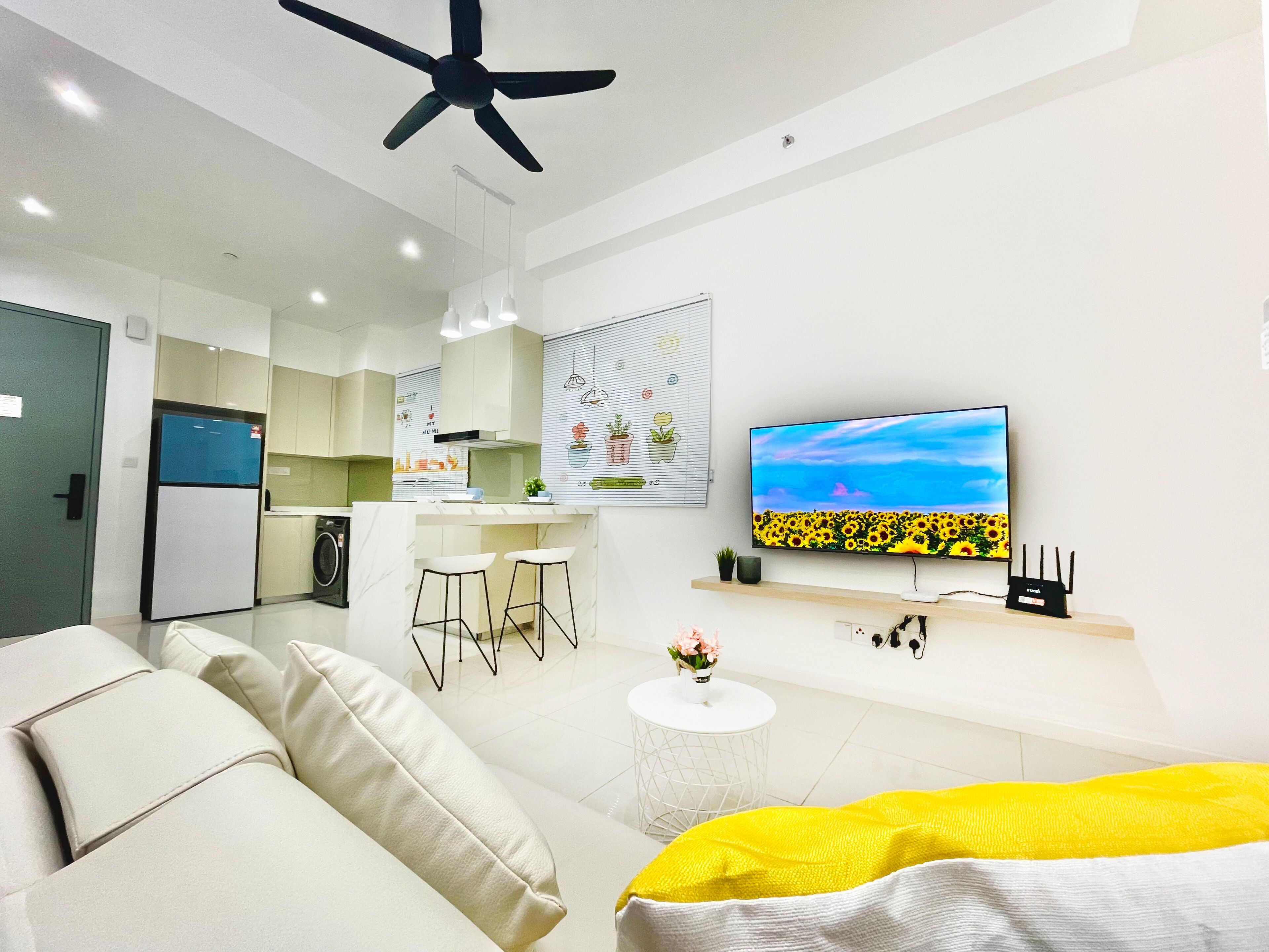 A modern living room with a sofa, a yellow blanket, a TV, and a kitchen in the background.