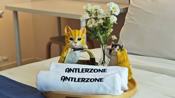 Una cama con una almohada blanca, una toalla blanca con la leyenda "ANTLERZONE" y un pequeño florero con flores blancas.