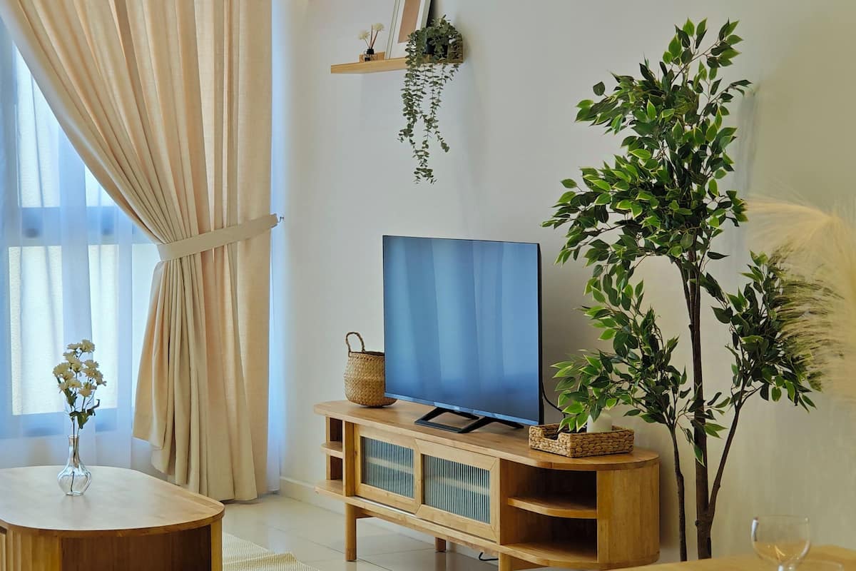 Ein Wohnzimmer mit Fernseher auf einem Holzboden, einem kleinen Tisch mit einer Vase und einer großen Pflanze.