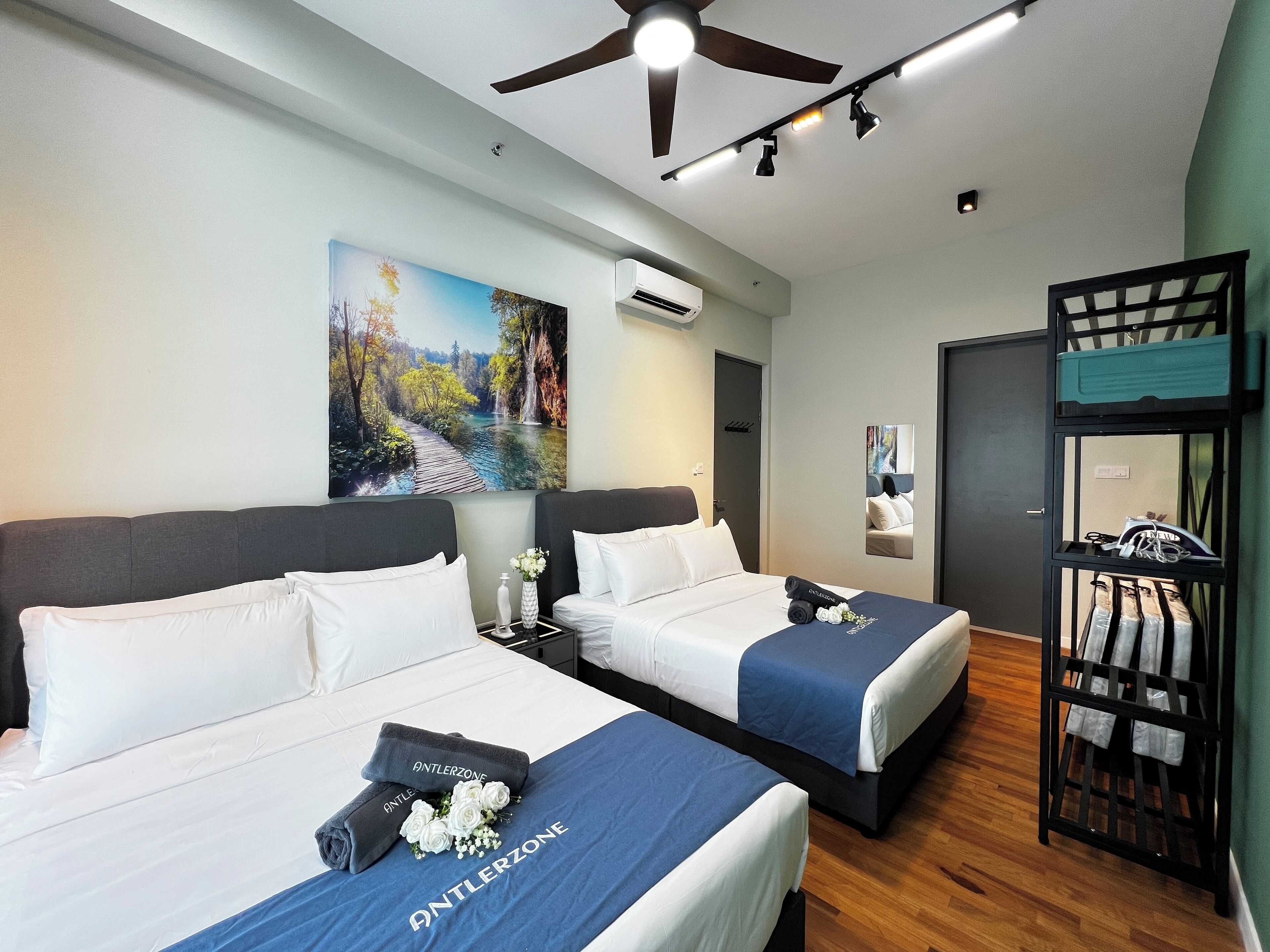 Una habitación de hotel con dos camas, un ventilador de techo, un equipo de aire acondicionado, un cuadro en la pared y un espejo.