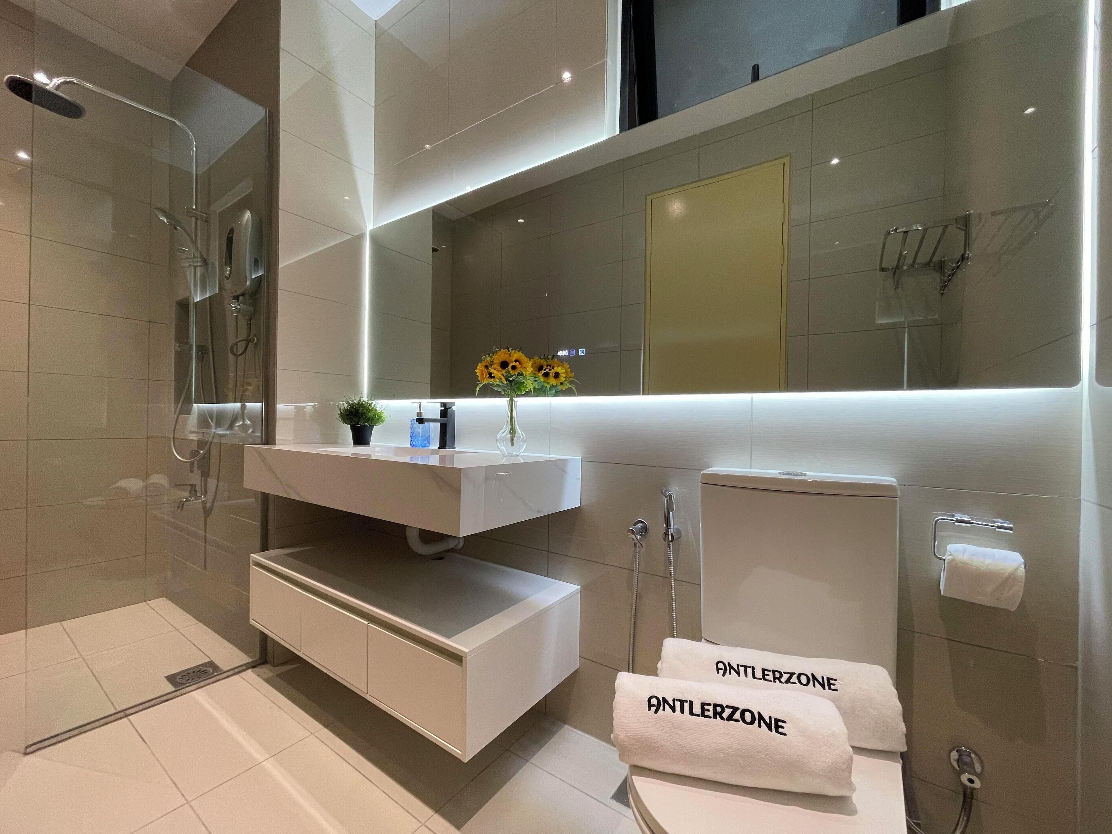 A modern bathroom with a glass-enclosed shower, a white vanity with a mirror, and a towel rack with towels labeled "ANTLERZONE".