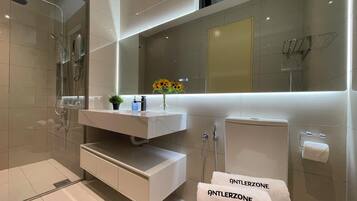 A modern bathroom with a glass-enclosed shower, a white vanity with a mirror, and a towel rack with towels labeled "ANTLERZONE".